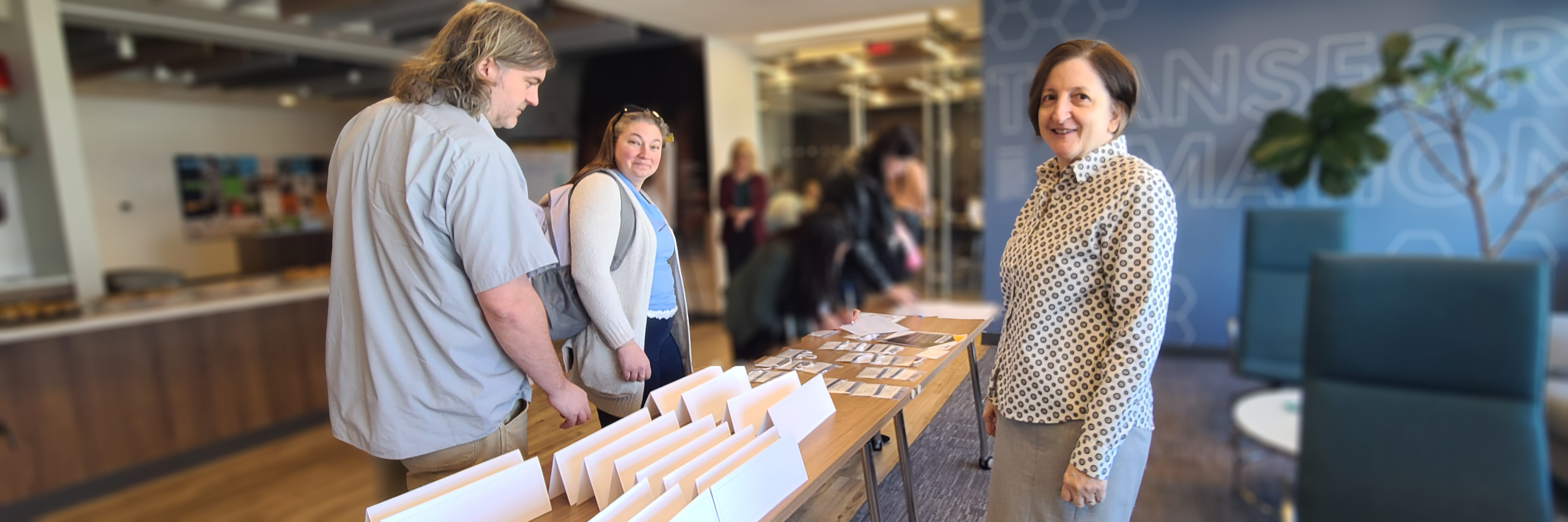 A woman stands behind a registration table while a man and another woman register New Directors Orientation 2026-04-10