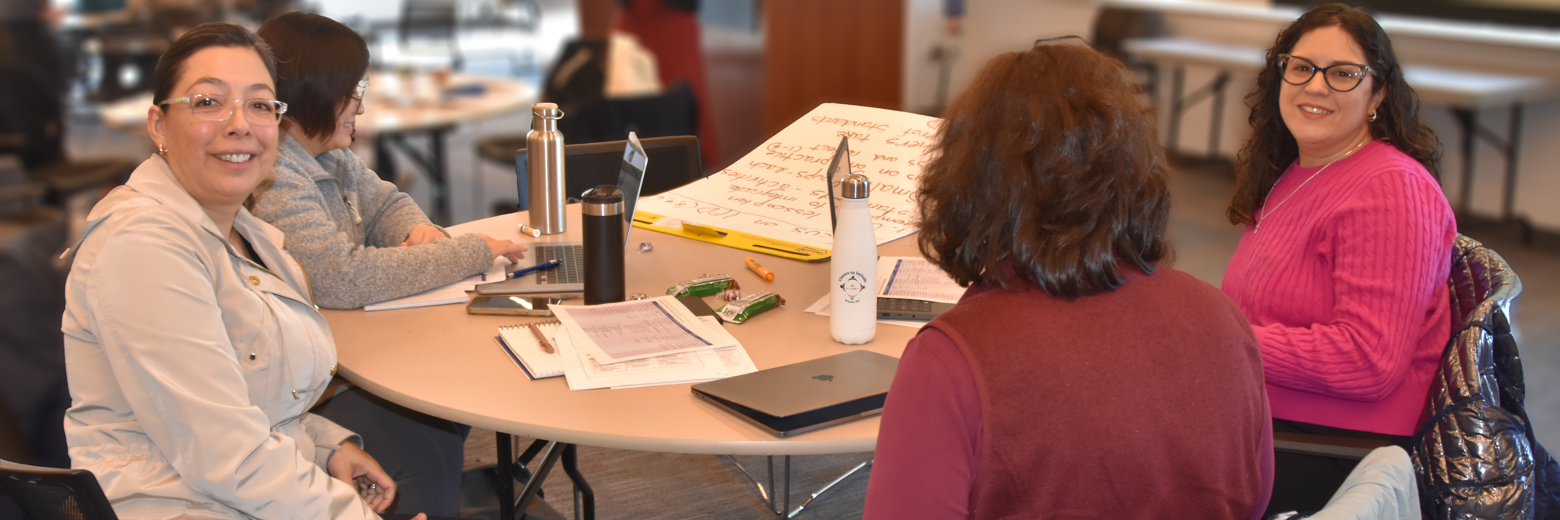 Four women participants around a round table at the 12/12/25 New Directors' Orientation. Two are looking at the camera.