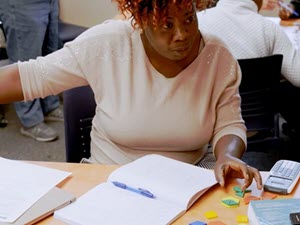 A woman at a table with a pad of paper and a pencil on the table in front of her.