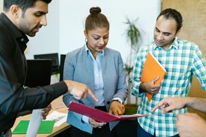Three adult students standing, looking at a notebook one is holding