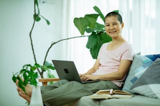 smiling woman on couch studying using laptop