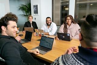 small office team at a table with laptops looking at someone in the front of the room